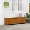 A wooden storage bench with two pillows on top, placed on a patio next to a white wooden wall with a window. Produktbild-Vorschau