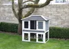 A two-story wooden hutch for small animals is situated on a grassy lawn in front of a stone wall and a tree. Voir les images du produit
