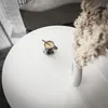 A close-up view of a white round coffee table with a cup of coffee and a vase with dried flowers. Produktbild-Vorschau