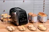 A black bread maker is displayed on a wooden table with various baked goods, including muffins, rolls, and loaves of bread, arranged around it. Podgląd zdjęcia produktu