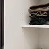 A close-up view of folded clothes on a shelf inside a wardrobe. Produktbild-Vorschau