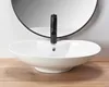 A white vessel sink with a black faucet is shown in a bathroom setting with a round mirror in the background and a wooden surface in the foreground. Náhled obrázku produktu