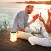 A couple is sitting on a wooden dock by the water at sunset, eating watermelon. A solar lantern is placed on the dock next to them. Produktbild-Vorschau
