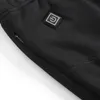 Close-up of a black garment, likely pants or a base layer, showing a zipper pocket and a power button icon. Podgląd zdjęcia produktu