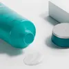 A close-up shot of a teal tube of hair product with some product squeezed out onto a white surface, and a teal jar with a silver lid in the background. Náhled obrázku produktu
