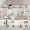 A woman is cooking in a modern kitchen with a set table in the foreground. Produktbild-Vorschau