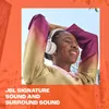 A woman wearing headphones and smiling with her hands behind her head, with buildings in the background. Voir les images du produit