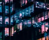 A close-up view of a modern office building at night, with illuminated windows showing desks and computer monitors. Voir les images du produit