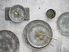 A top-down view of a set of stoneware plates and cutlery on a textured gray surface. Náhľad obrázku produktu