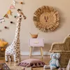 A child's bedroom with a giraffe stuffed animal, a woven lion wall decoration, and a pink nightstand. Produktbild-Vorschau