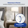 A white table fan is shown on a bedside table next to a lamp and bed. Podgląd zdjęcia produktu