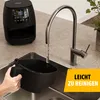 A person is cleaning an air fryer basket under a faucet in a kitchen sink. Produktbild-Vorschau