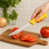 A hand is shown slicing a tomato on a wooden cutting board with a yellow-handled knife. Other ingredients like an onion and parsley are visible in the background. Produktbild-Vorschau