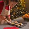 A woman is decorating Christmas cookies with a piping bag in front of a decorated Christmas tree. Anteprima dell’immagine prodotto