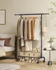 A bedroom scene with a clothing rack filled with clothes, a bed, and a small side table. Produktbild-Vorschau