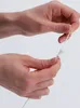Hands holding a white object with a string attached. Náhľad obrázku produktu