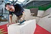 A man is using a jigsaw to cut a piece of wood in a workshop. Voir les images du produit