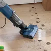 A blue and gray Shark Hydrovac wet dry vacuum cleaner is being used to clean muddy paw prints off a light wood floor. A yellow and green tennis ball is visible in the bottom left corner. Podgląd zdjęcia produktu