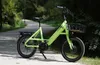 A lime green electric bicycle is parked on a paved path in a park-like setting. Produktbild-Vorschau