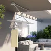 A retractable clothes drying rack is mounted on a ceiling on a balcony, with clothes hanging on it. There are sofas and plants in the background. Podgląd zdjęcia produktu