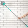 A person's arm is holding a long-handled cleaning brush against a white tiled wall. Podgląd zdjęcia produktu