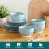 A set of blue and white ceramic dishes, including plates and bowls, arranged on a wooden table with a plant in the background. Náhled obrázku produktu