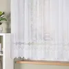 A white lace curtain with a decorative hem hangs in front of a window. Náhled obrázku produktu