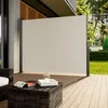 A retractable side awning is set up on a wooden deck next to a house, with a coffee table in the foreground. Anteprima dell’immagine prodotto