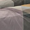 A close-up view of a patterned fabric, likely bedding, with geometric shapes and stripes in various shades of gray, purple, and brown. Produktbild-Vorschau