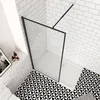 A modern bathroom shower enclosure with black framing and clear glass, set against white subway tiles and a black and white geometric floor. Produktbild-Vorschau