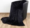 A black blanket draped over a black armchair, with the blanket extending onto a wooden floor. Produktbild-Vorschau