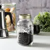 A Kilner jar filled with coffee beans is displayed on a white surface, with a moka pot and a jar of cookies in the background. Podgląd zdjęcia produktu