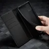 A hand is holding a black phone case over an open black wallet. Produktbild-Vorschau