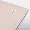 A close-up shot of a light pink swaddle blanket with a small brand tag attached. Náhľad obrázku produktu