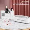 A white makeup organizer and a white cleaning machine are displayed on a marble table, with a pink curtain in the background. Produktbild-Vorschau