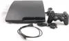 A black Sony PlayStation 3 console with its accessories laid out on a white background. Produktbild-Vorschau