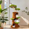 A cat tree with multiple levels and platforms, featuring three cats lounging on it, placed in a well-lit room with plants and a window. Produktbild-Vorschau