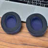 Two blue and black ear pads are placed on a wooden surface in front of a laptop. Podgląd zdjęcia produktu