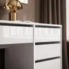 A close-up view of a white desk with drawers and a gold lamp on top. Produktbild-Vorschau