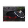 A red metallic wok with a glass lid is placed on a dark, textured surface, with a green plant in the background. Náhled obrázku produktu