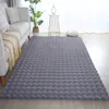 A grey fluffy rug is placed on a wooden floor in a living room setting, next to a sofa and a small side table with a plant. Produktbild-Vorschau