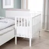 A white crib attached to a larger bed in a room with light blue walls and white curtains. Produktbild-Vorschau