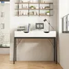 A white desk with black legs and drawers, placed against a white wall with shelves above it. Náhled obrázku produktu