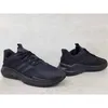A pair of black Adidas sports shoes are displayed against a light gray concrete background. Produktbild-Vorschau