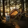 A couple is sitting in camping chairs in front of a tent, with a portable toilet in the foreground. Anteprima dell’immagine prodotto