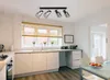 A modern kitchen with white cabinets, a window with blinds, and a black track light fixture with four adjustable spotlights. Produktbild-Vorschau