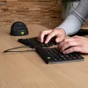 A person's hands typing on a split ergonomic keyboard on a wooden desk. Produktbild-Vorschau