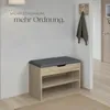 A shoe bench with storage is placed in an entryway next to a wall with text and a coat rack with a jacket. Náhled obrázku produktu