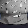 A close-up view of a grey baby carrier with a feather pattern, showing a pocket with a white smartphone inside. Náhled obrázku produktu