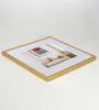 A gold picture frame with a white mat and a picture of a red flower on a blue background inside. The frame is shown at an angle on a white surface. Produktbild-Vorschau